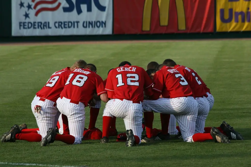 High school baseball team kneeling together in prayer on a natural grass field before the first pitch