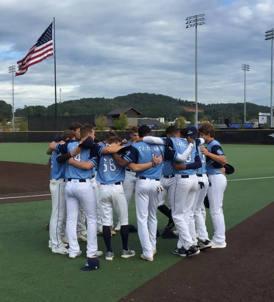 Youth baseball team kneeling in prayer on the field with an American flag in the background