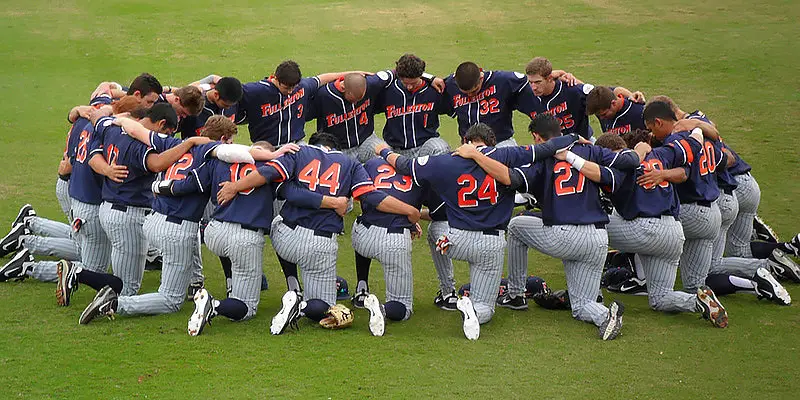 Baseball team kneeling together in prayer before the first pitch, viewed from above